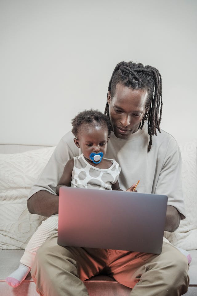 A father and 3-year old daughter sit with a laptop computer.